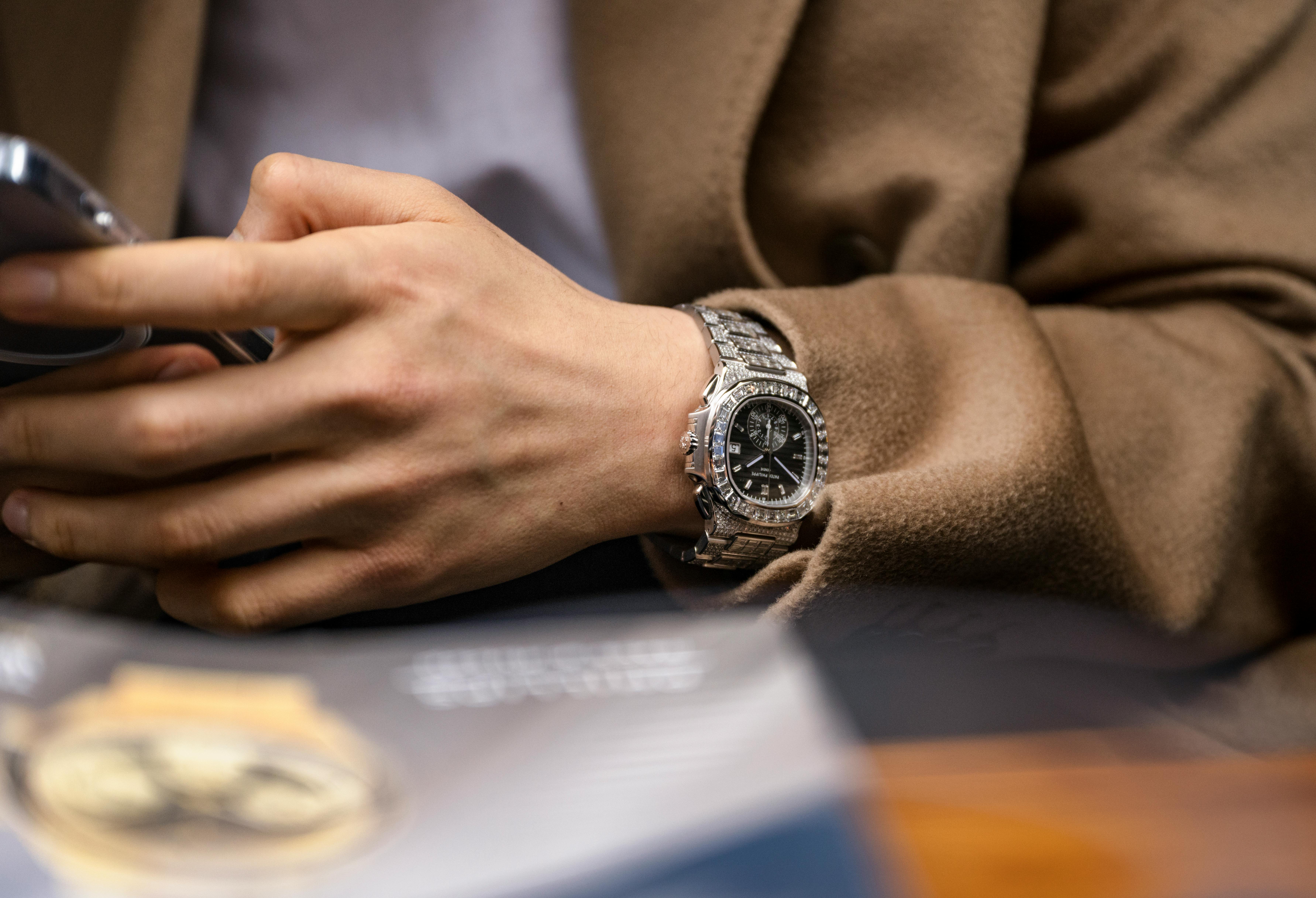 A man in a tan coat wears a Patek Philippe Nautilus 5980-1400G