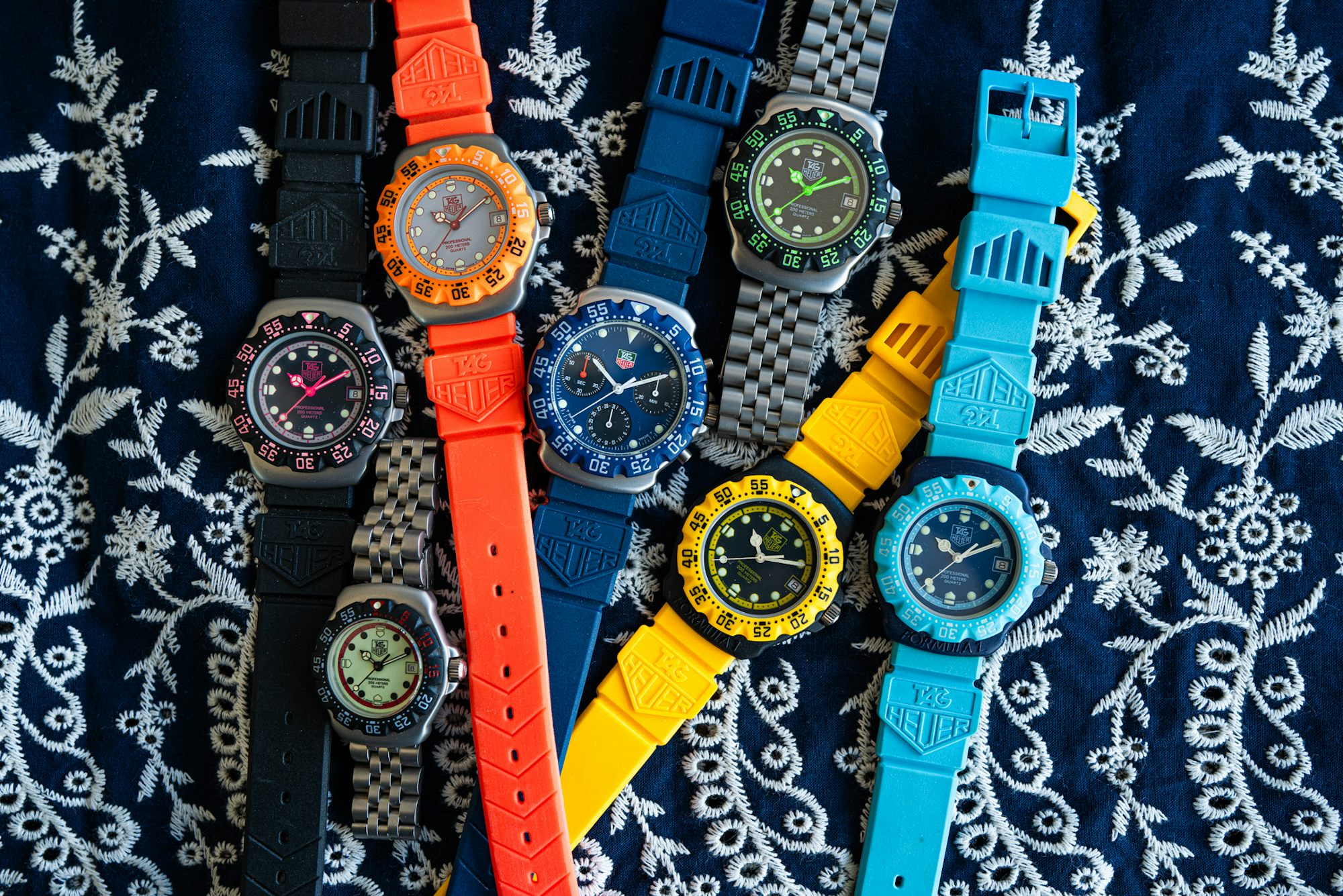 A collection of brightly colored watches laid out on embroidered fabric