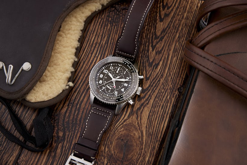 A brown IWC pilot's watch lays on a wooden surface.