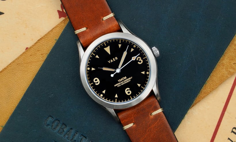 A black dial field watch with tan accents on a leather strap.