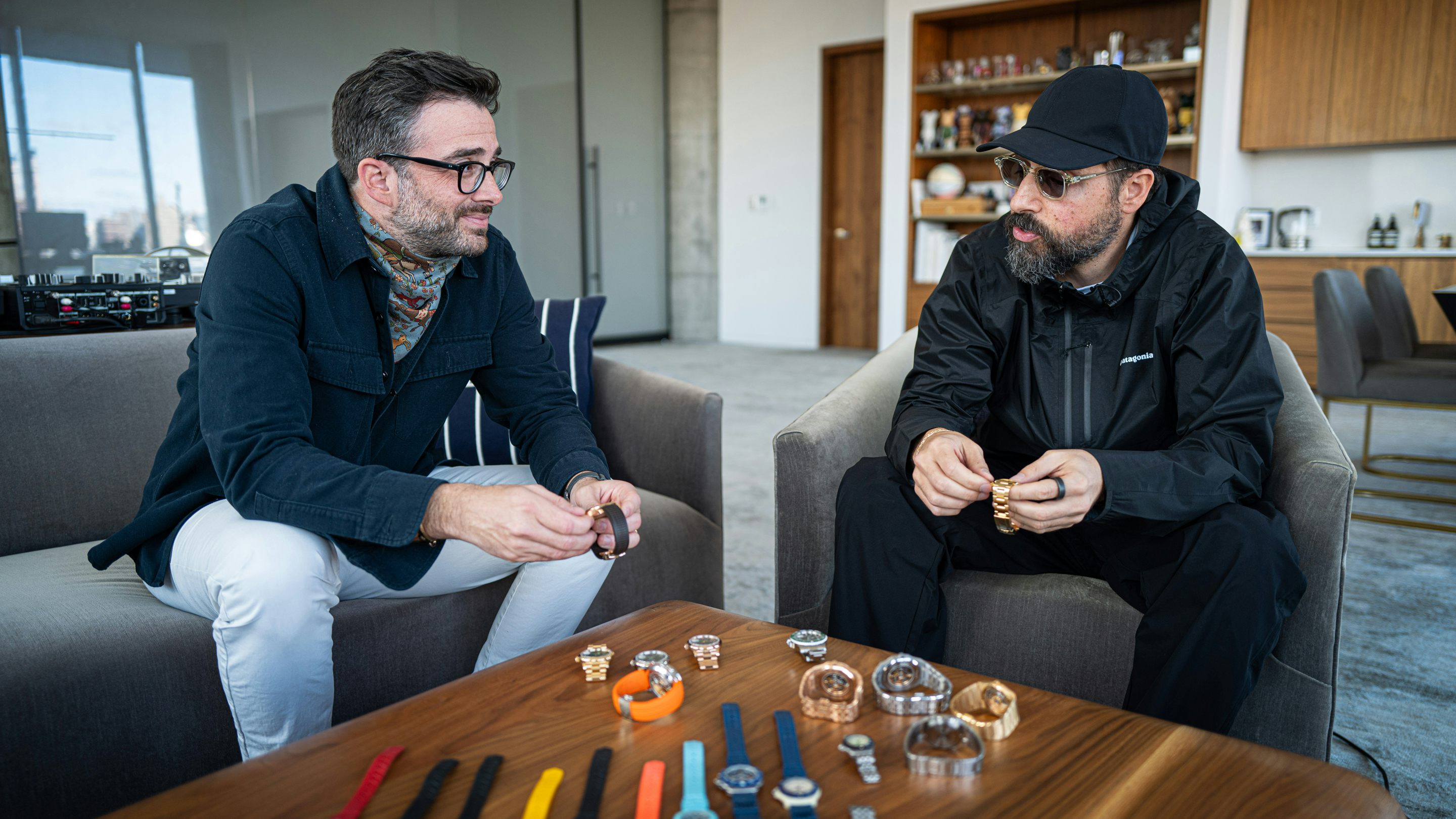 Hodinkee founder Benjamin Clymer and KITH owner-operator Ronnie Fieg sit side by side in a large office space discussing the watch collection on the table in front of them