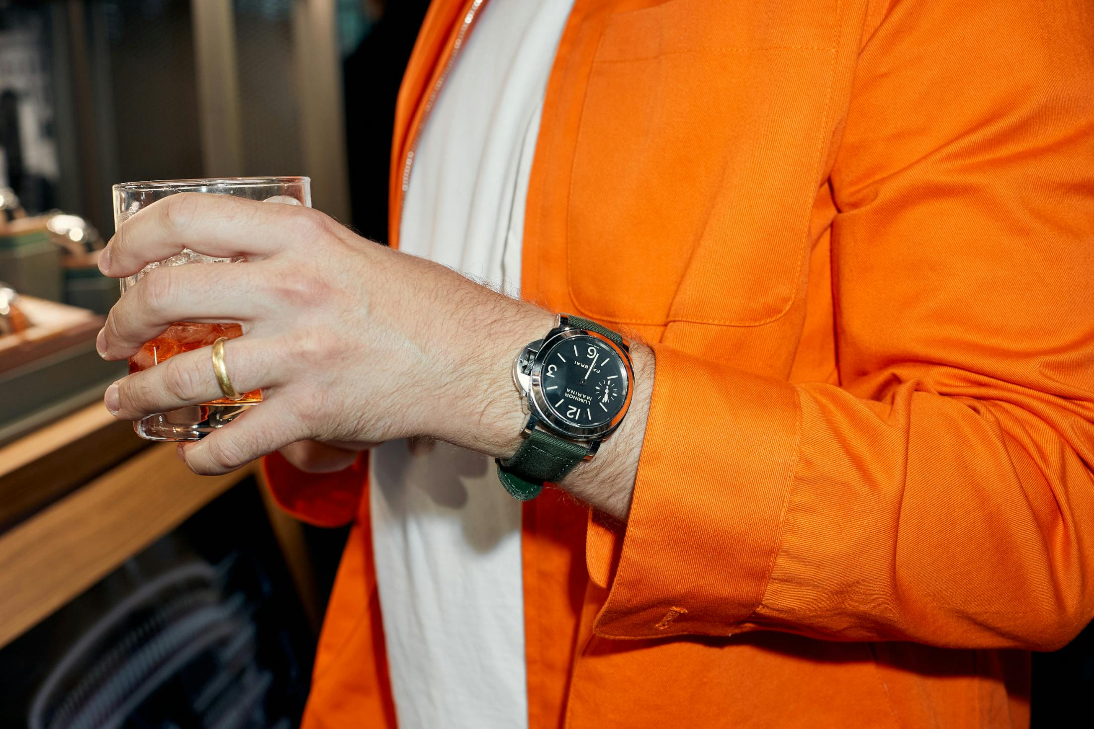 Someone in orange jacket holds a cocktail with a watch on wrist