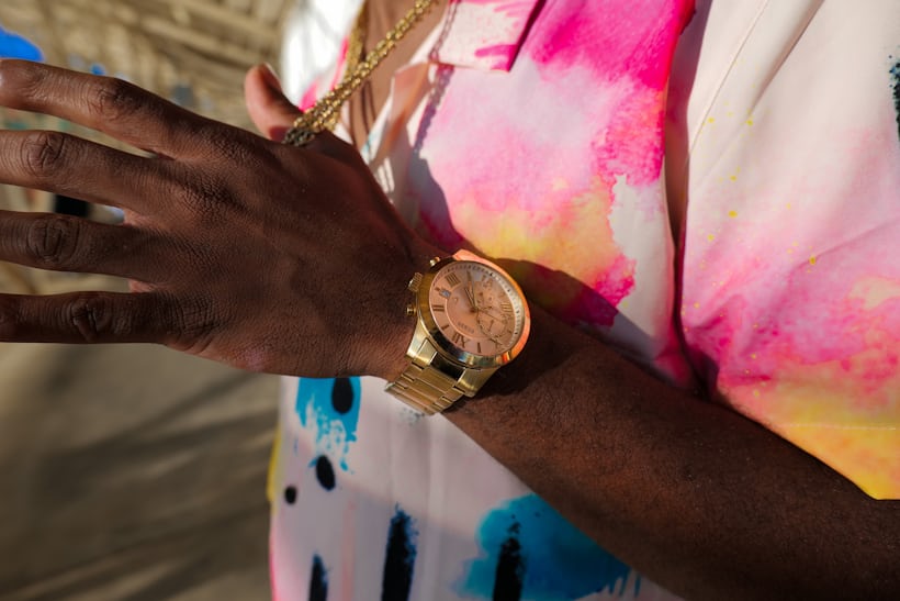 A person wearing a gold watch and tie dye shirt