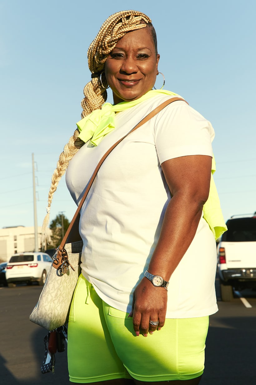 A woman posing in a parking lot with a watch and purse