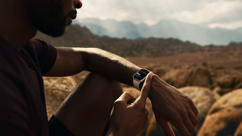 A man checks his Apple Watch while sitting in the desert.