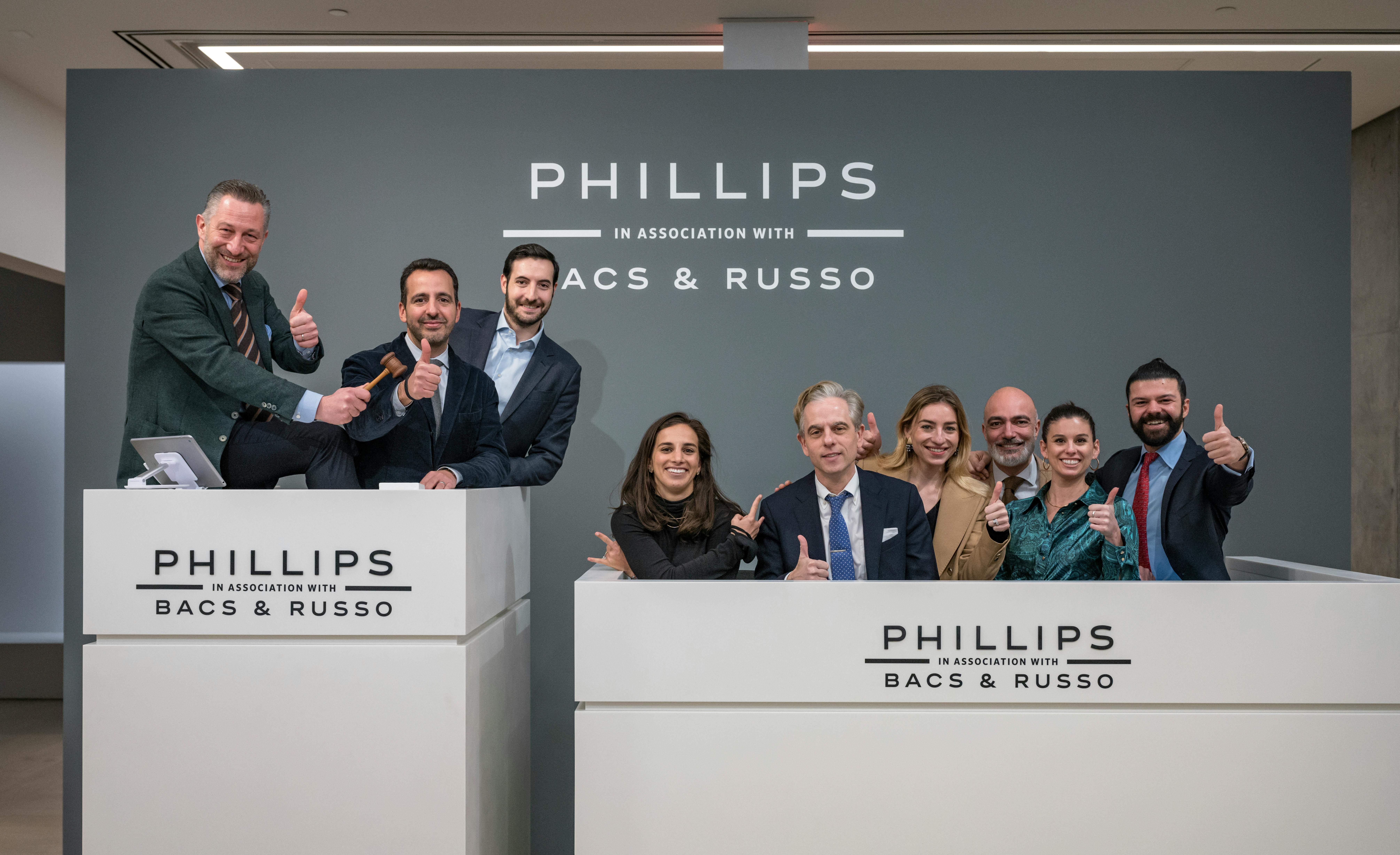 A group of nine people stand smiling at an auction podium. 