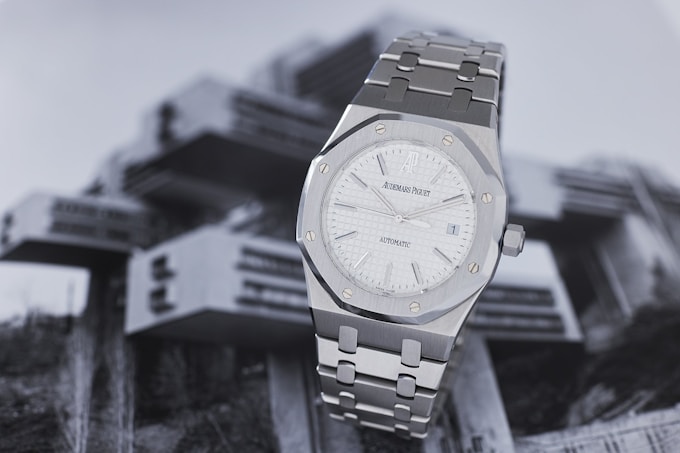 An Audemars Piguet Royal Oak with a white dial sits on a greyscale photograph of a building.