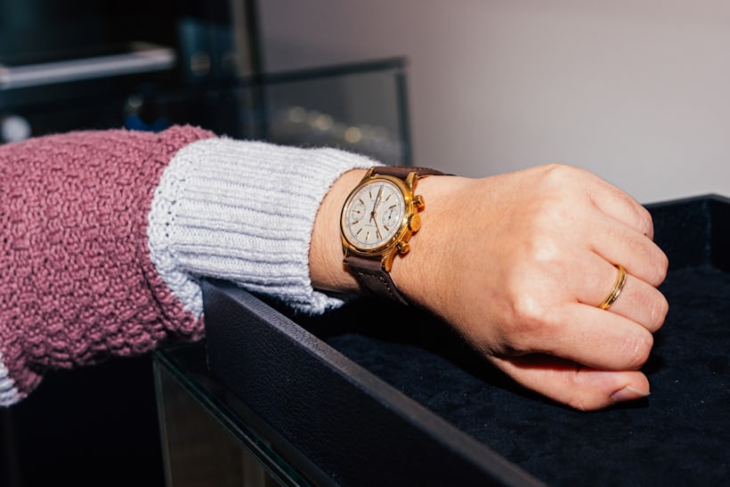 A wrist wearing a watch and a white and pink sweater