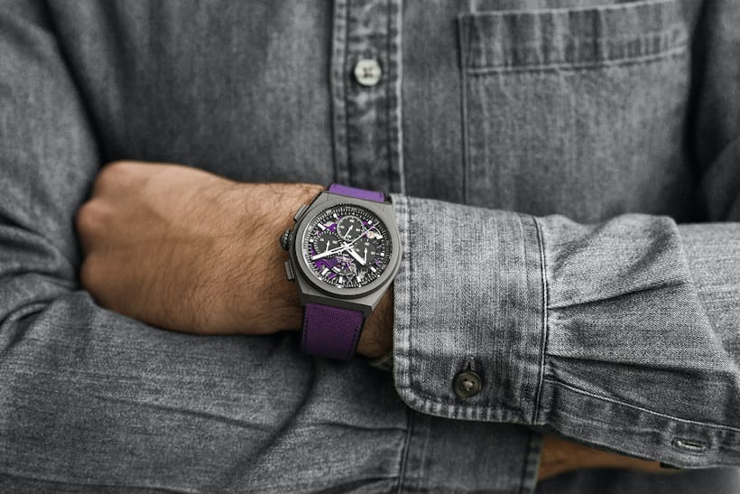 A wristshot of a man wearing a Zenith Defy 21 Ultraviolet in a purple jacket. 