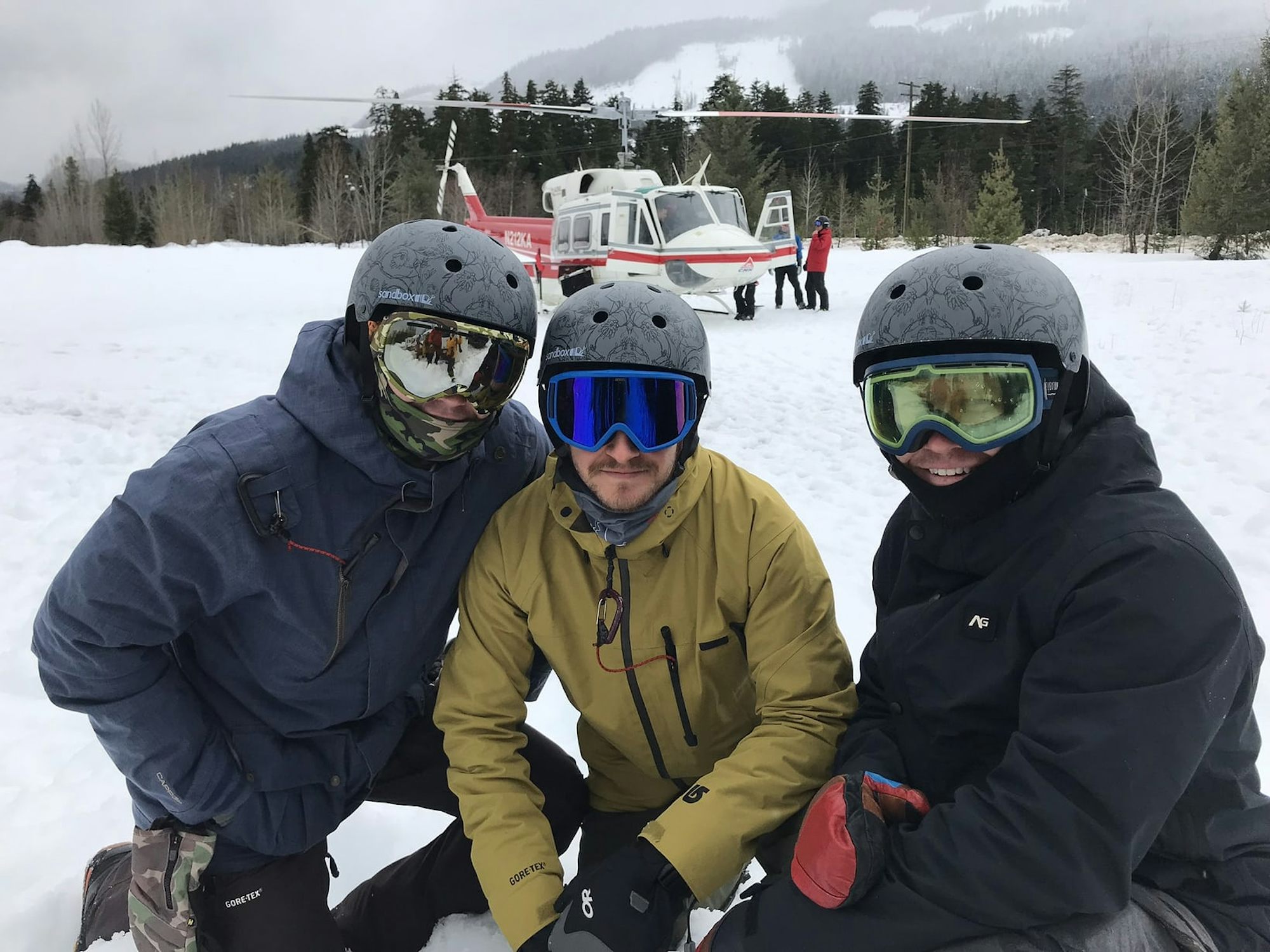 Three men in the snow with a helicopter in the background