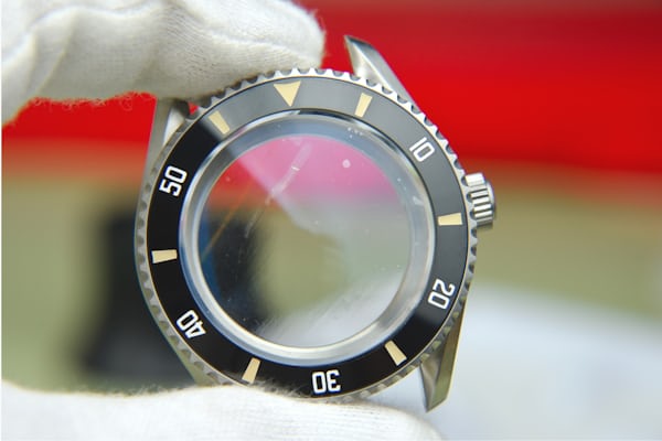 A watchmaker holds an assembled case, bezel, and crystal.
